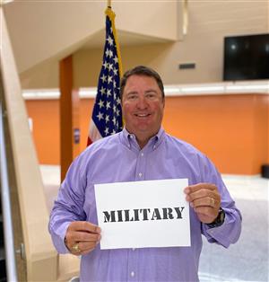 Principal Shannon Brown at Liberty Middle in purple shirt holding sign thanking military 